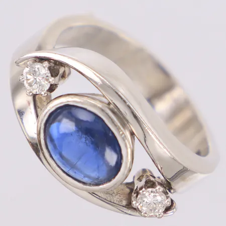 Ring med cabochonslipad blå safir, repor, och briljantslipade diamanter 2xca 0,10ct, stl:17¾, bredd 11,4mm, signerad Elon Arenhill, Brösarp, år 1982, skadad fog i skenan, sten löst infattad, vitguld, 18K Vikt: 11,3 g
