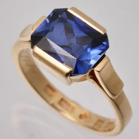 Ring i 18K guld, stl18½, bredd 3-11mm, 1st blå sten, mått 8,9x11mm, personlig gravyr, spricka i skena, tillverkad av Emil Lindqvist, år 1921, bruttovikt 7,97g, ca nettovikt 7g.