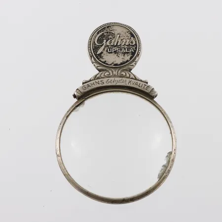 Förstorningsglas vitmetall,reklam för Gahns Upsala,diameter ca 5 cm,kantskada på glaset.