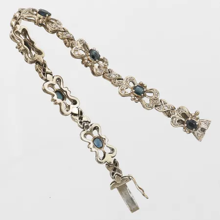 Armband med mörkt grönblå (tealfärgade) safirer, slitage/nagg, åttkantsslipade diamanter 70 x 0,01ct samt 7 x 0,02ct, längd 18cm, bredd 10mm, trasigt/defekt kistlås,18K vitguld, vikt 29,1gram Vikt: 29,1 g