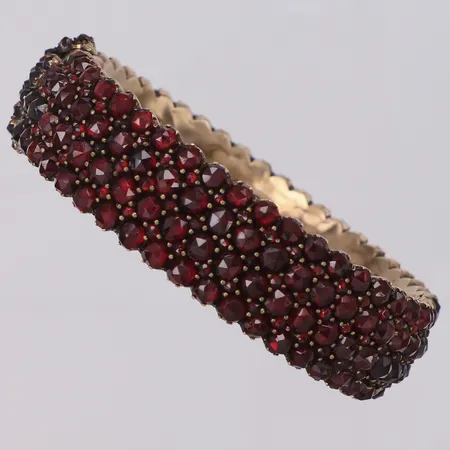 Stelt armband med granater Ø55mm, bredd 15,7mm, gravyr: Till minne 1877, öppningsbart, glapp i lås, bucklig på insidan, saknar en sten, ostämplad gulmetall/silver  Vikt: 38,2 g