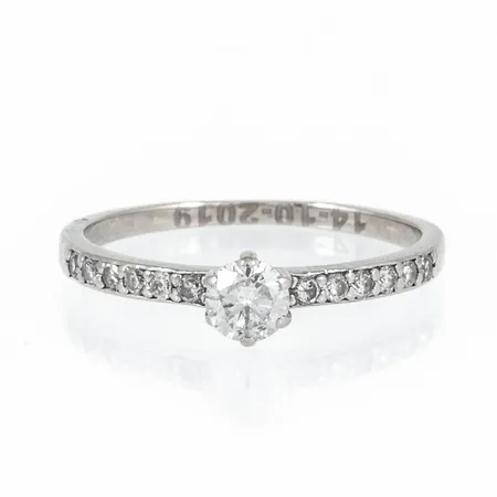 Ring med 1 x ca 0,25ct och 12 x ca 0,01ct diamanter stl:17 bredd 1,3-5mm, gravyr, flera nötta klor, vitguld 18K 1,7g.