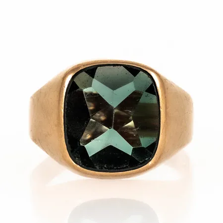 Klackring i 18K guld med grön sten (syntetisk spinell). Den är i storlek 20, är 3 - 15 mm bred och väger 5,0g. Skev skena, repig sten. 