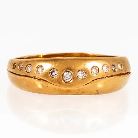 Doserad ring i 18K guld med 1 x c:a 0,03ct, 2 x c:a 0,02ct, 4 x c:a 0,015ct och 3 x c:a 0,01ct briljantslipade diamanter i riven fattning. Den är i storlek 20, är 3 - 7,5 mm bred och väger 4,7g. En sten saknas.
