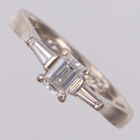 Ring med smaragdslipad diamant 1xca0,40ct samt trapetsslipade 2xca0,07ct, stl 16¾, bredd 1,7-5,4mm, vitguld, gravyr, 18K Vikt: 3,2 g
