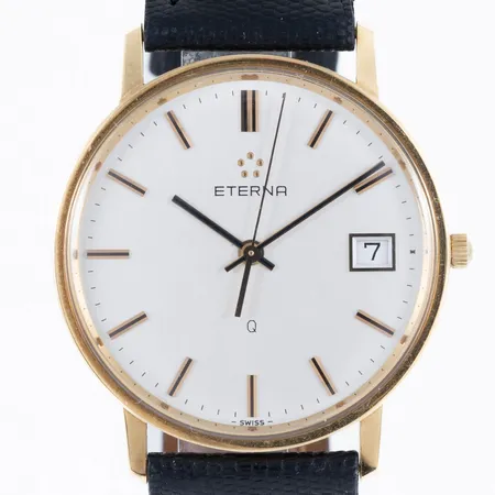 Herrur Eterna Q i 18K guld med band i svart läder. Boett Ø 33,5 mm, datum, gravyr (initialer). Går ej - Batteribyte krävs? Bruttovikt: 26,6g. 