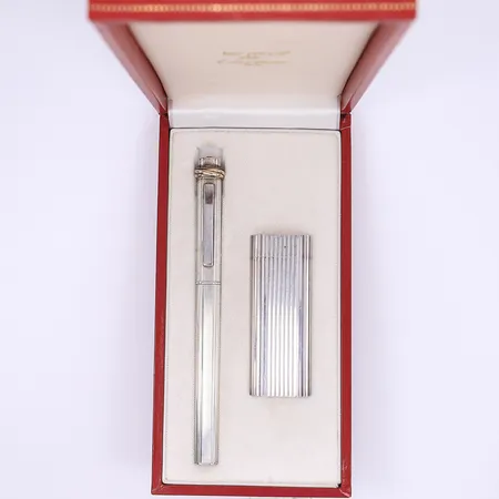 Penna och tändare Les Must de Cartier, penna Trinity kulspets 13,5cm serienummer 232399, i behöv av nytt bläck, made in France, tändare 7cm serienummer 93602G, ej testad med gas, Swiss Made, vitmetall, smärre bruksslitage, i etui