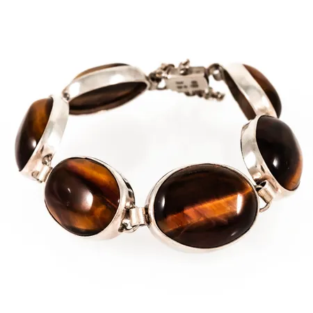 Armband i silver med tigeröga. Det är 19 cm långt, 17,7 - 20,2 mm brett och har kistlås och säkerhetskedja. Stämplat VJ (Victor Janson), Lindesbergs stadsstämpel, kattfot, S, Z9 (1974). En extralänk / sten medföljer som blir 3 cm lång. Total bruttovikt 47,2g.