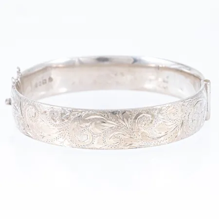 Stelt öppningsbart armband i silver. Graverad dekor på ena halvan. Det är 12,7 mm brett, har ett innermått på 18 cm och väger 23,2g. Istickslås. Tomma öglor efter säkerhetskedja. Engelska tillverkarstämplar. Vikt: 23,3g.