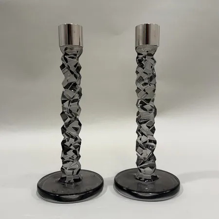 Ett par Ljusstakar "Carat" formgivna av Lena Bergström för Orrefors rökfärgade, höjd ca 24 cm, fotplatta Ø10cm, ljushållare i rostfritt stål, ena saknar etikettmärkning, mindre repor samt färgbortfall undertill