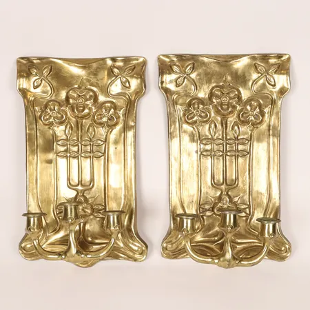 Ett par ljusplåtar jugendstil, mässing, omkring år 1900, dekor av stiliserade blommor i relief, vardera med tre ljusarmar, höjd 40cm, bredd 25cm, djup ca 15cm, åldersbetingat slitage. Skickas med postpaket.
