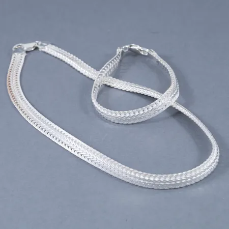 Set i halvstelt delvis matterat silver. Collier 42 cm, armband 20 cm. Bredd 8,2 mm. Stämplat 925. Framstår oanvänt. Vikt: 49,8g.