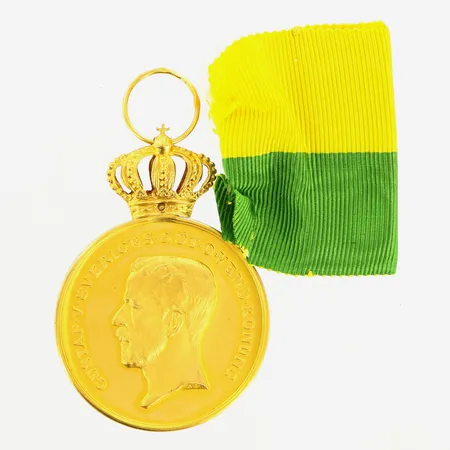 Medalj för långvarig och trogen tjänst, Kungliga Patriotiska Sällskapet, längd 50mm, bredd 36mm, gravyr, krona och ögla i 18K, medalj i 23K, bruttovikt: 29,1gram Vikt: 29,1 g