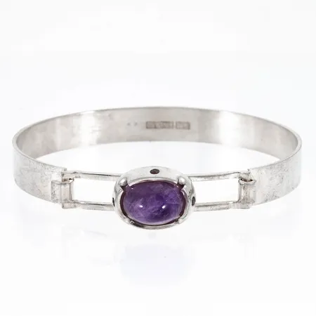 Armband i silver med en cabochonslipad ametist. Innermått 17 cm. Bredd 8 - 13,4 mm. Stämplat 830 FINLAND. Gravyr "1967" på undersidans utsida. Vikt 18,6g.