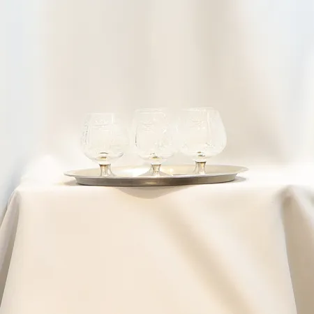 Serveringsbricka i silver Ø26cm samt 6st Cognacglas med fot i silver höjd: ca10cm kupor i kristallglas, troligen gjuten dekor, brickans vikt 379,2g silverhalt 800/1000 (polska stämplar) samt glasens fötter i 900/1000 (ej stämplade) total bruttovikt 1275,4g, kommer med etui