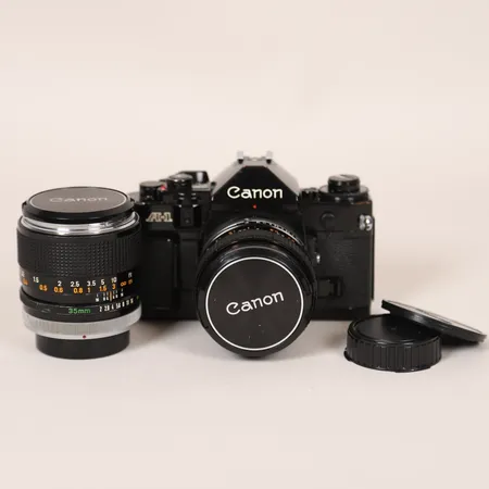 Kamera Canon A-1, svartlackerad, serienummer 936229, tidigt 70- tal, med body cap, med två objektiv: Objektiv Canon FD 50mm 1:1.4, serienummer 341235, linsskydd, 1 Objektiv Canon FD 35mm 1:2, serienummer 21938, linsskydd, samtliga ej funktionstestade, smärre bruksslitage, hus med några märken och ytliga repor.