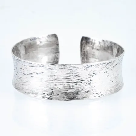 Konkav armring i silver (925/1000) med mönsterdekor. Innermått 20,5 cm (inkl öppning 13 mm), 22,5 mm bred och väger 41,1g. Stämplad D10, 925 och kattfot. Gravyr (initialer och datum)