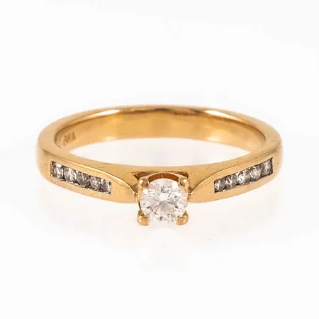 Ring i 18K guld med 1 x c:a 0,15ct och 10 x c:a 0,01ct (c:a W/si) briljantslipade diamanter. Den är i storlek 16, är 2,6 - 3,7 mm bred och väger 3,4g. Stämplad GHA (Guldfynd), 18K.