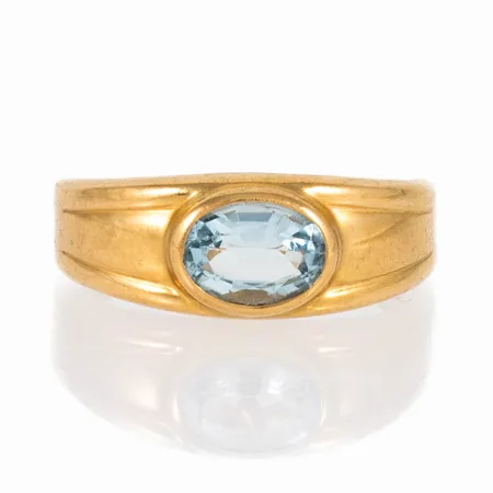 Ring i 18K guld med ljusblå sten. Den är i storlek 17, är 2 - 7 mm bred och väger 1,9g. Gravyr (datum). Något ojämn skena. 