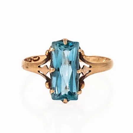 Ring i 14K guld med turkosblå (syntetisk) sten 5,5 x 12 mm. Den är i storlek 18¼, är mm bred och väger 1,8g. Gravyr, naggade fasetter på sten. 