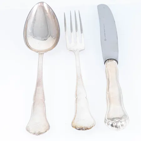 Finsk Chippendale i silver (830/1000) 12 skedar 170 mm, 12 gafflar 160 mm, 12 knivar med rostfria blad 195 mm. Finska stämplar med svenska importstämplar. Skedar & gafflar 738g. Knivar 840g bto. Bruksskick. Skickas med postpaket.
