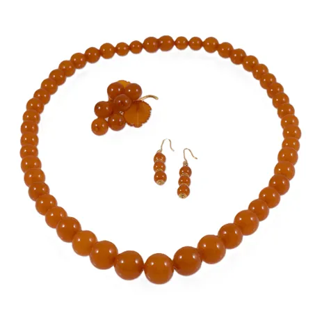 Set med bärnsten: Collier längd 62cm bredd 10-18mm, skruvlås. Brosch vindruvsklase 42x54mm gulmetall. Örhängen bredd 8mm längd inkl krok 52mm gulmetall. Total bruttovikt: 77,7g.