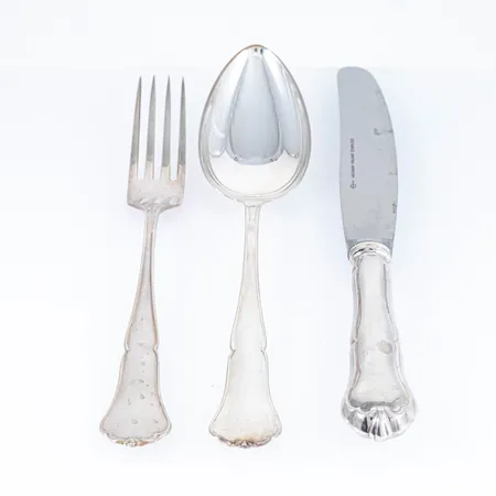 Finsk Chippendale i silver (830/1000) 12 skedar 185 mm, 12 gafflar 175 mm, 12 knivar med rostfria blad 205 mm. Finska stämplar med svenska importstämplar. Skedar & gafflar 998g. Knivar 884g bto. Bruksskick. Skickas med postpaket.