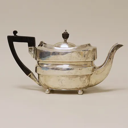 Tekanna med trähandtag höjd ca 11cm bredd ca 22x9cm, bucklor otydliga stämplar, troligen England, silver 830/1000  Vikt: 232,6 g