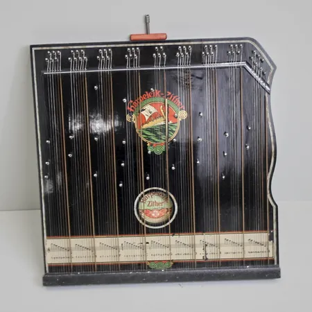 Bordscittra Harpelik-Zither, tillverkad i Sachen Tyskland, stämnyckel medföljer, 5 strängar saknas, färgbortfall på dekor på notremsa. Vikt: 0 g Skickas med postpaket.