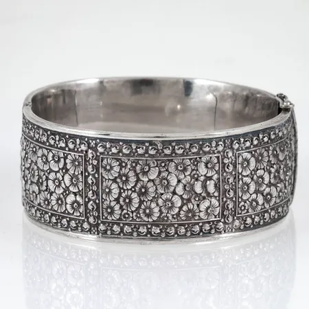 Stelt armband med blomsterdekor. Bredd 27 mm. Innermått 18,5 cm. Små ojämnheter. 43,5g silver 925/1000.