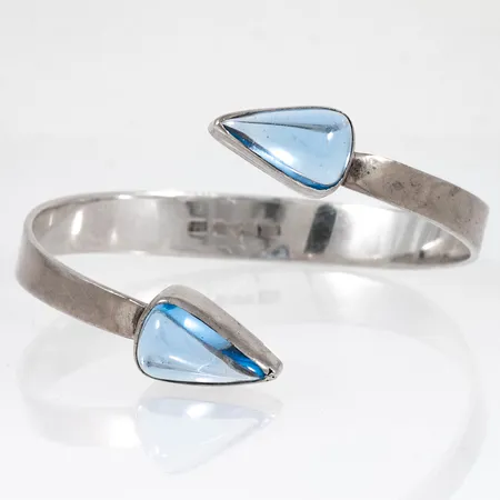Stelt armband med ljusblå stenar. Bredd ca 9 - 35 mm. Innermått ca 18,5 cm. Tillverkat 1962 av Kjellins Guld i Umeå. Silver 23,4g. 