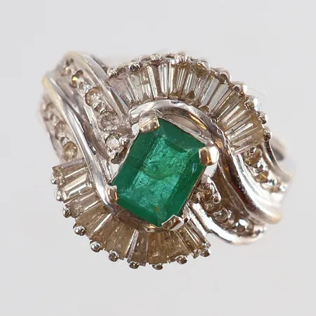 Ring med smaragd 7,1x5,2mm samt diamanter 14 x 0,01ct 20 trapetslipade diamanter smaragd med inneslutningar som når ytan litet nagg stl:16½ bredd 3-16,5mm vitguld 18K. Vikt: 7 g
