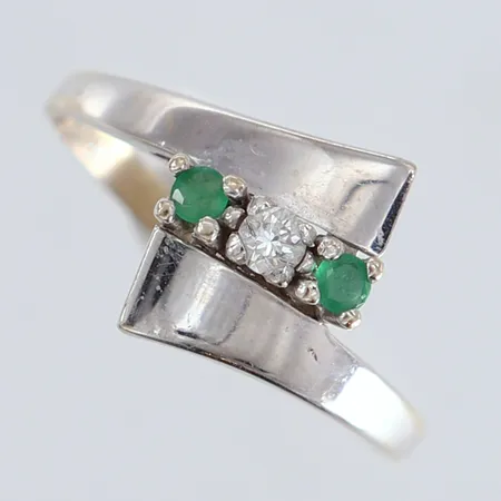 Ring med diamant 1 x 0,05ct samt gröna stenar stl:17½ bredd 12mm skev skena vitguld 18K. OBS Ändrad beskrivning 2026-09-23 Vikt: 2,6 g