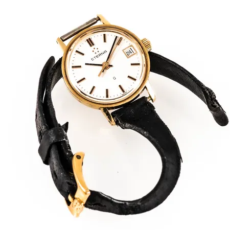 Damur Eterna guld 18K quartz Ø22mm, datum, plexiglas, med svart läderband (defekt), repigt glas, gravyr, går ej - batteribyte krävs? Bruttovikt 12,6g.