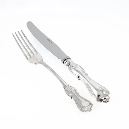 12 bordsgafflar i silver (830/1000) av modellen Olga, längd c:a 179 mm, vikt 489,4g. 12 bordsknivar i silver (830/1000) av modellen Olga, längd c:a 210 mm, blad i rostfritt stål, fyllda skaft, bruttovikt: 914,3g.