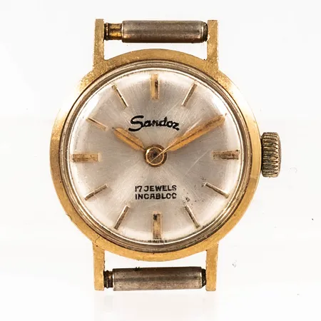 Damur Sandoz i 18K guld. Boett Ø 16,5 mm, manuell, repigt plexiglas, bucklig baksida. Bruttovikt: 5,4g.