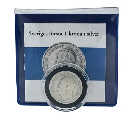 Silvermynt Oscar II 1 krona "Sveriges första 1-krona i silver" 1906 (utgivningsår 1876-1907), Ø25 mm, 80%, förvaras i myntkapsel liksom plastkonvolut från Mynthuset Sverige, informationsfolder Vikt: 7,5 g