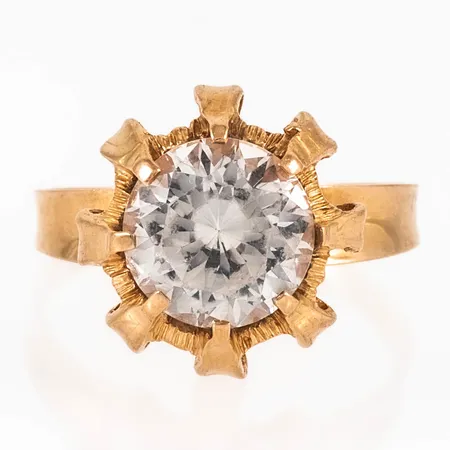 Ring i 18K guld med vit (syntetisk) sten Ø 10 mm. Den är i storlek 20, är 2 - 15,5 mm bred och väger 5,4g. Stämplad Y9 (1973), ALTON, Falköping, 18K och kattfot. Något naggade fasetter, ojämnhet i skenan. 
