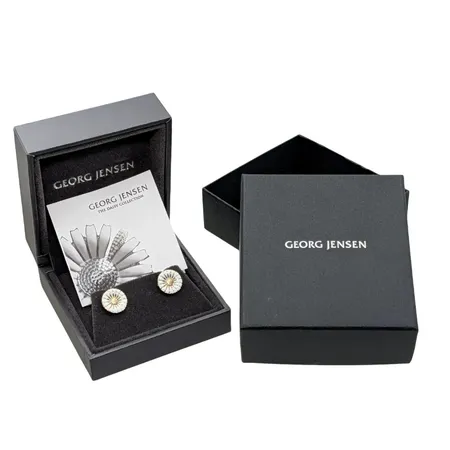 Örhängen, ett par "Daisy", GEORG JENSEN, silver 925/1000 (pläterade i 18K guld), vit felfri emalj, Ø11 mm, båda stämplade, originalploppar (stämplade GJ), originalask (65x70x35 mm) med yttre skyddsetui i papp + tillhörande informationsfolder "GEORG JENSEN THE DAISY COLLECTION", nyskick, sparsamt använda, nypris i butik från omkring 1750 :-  Vikt: 2,7 g