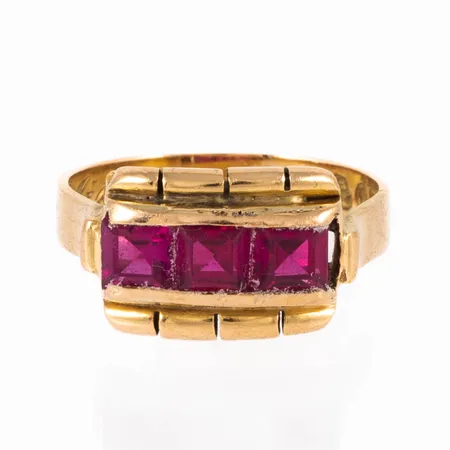 Ring i 18K guld med tre hallonröda (syntetiska) stenar á c:a 4,5 x 4,5 mm. Den är i storlek 16½, är 3,5 - 9 mm bred och väger 5,3g. Stämplad R9 (1967), BÅ (Åhlins Silversmide AB, Gällivare), 18K och kattfot. 
