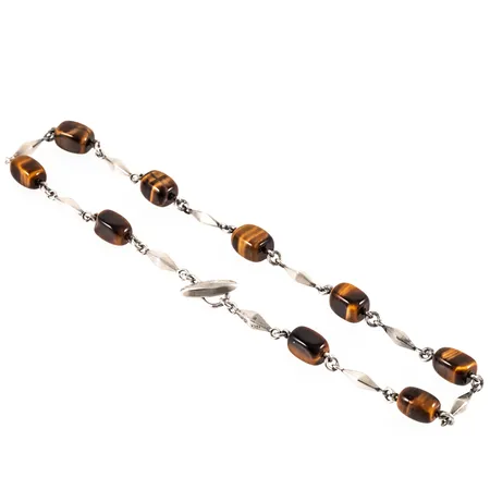 Colliér i silver med tigeröga. Det är 41 cm långt, 4 - 8,5 mm brett och väger 32,5g. Pinnlås. Stämplad S9 (1968), AMS (Arvo Saarela, Enköping), Silverstämpel & Kattfot.