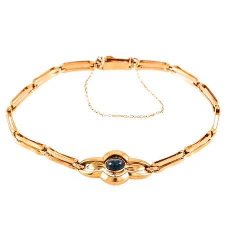 Armband i 18K guld med en cabochonslipad grön sten (sannolikt syntyetisk spinell) 4 x 5,5 mm. Det är 18,5 cm långt, 3,5 - 11,5 mm brett och väger 8,9g. Kistlås med säkerhetskedja. Vissa bucklor på länkar förekommer. 