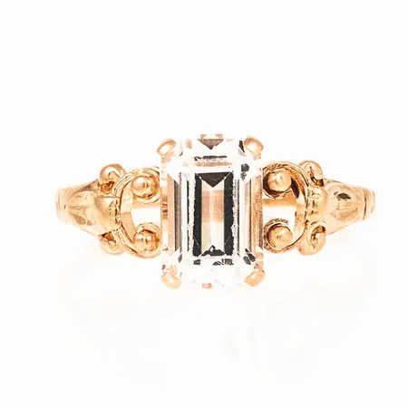 Ring i 18K guld med vit sten 9 x 6 mm (sannolikt syntetisk spinell). Den är i storlek 18, är 1,5 - 9 mm bred och väger 2,4g. Naggade fasetter på sten men fin lyster ändå. 