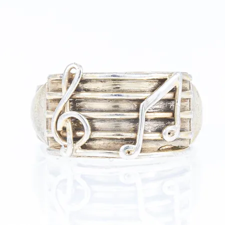 Ring i silver med dekor av noter. Den är i stolrek 18, är 4 - 11,5 mm bred och väger 5,9g. Stämplad Y8 (1949), AHN (Hanssons Guldsmedsaffär AB, Hässleholm), S och kattfot. Tidigare förgyllning delvis bortnött.