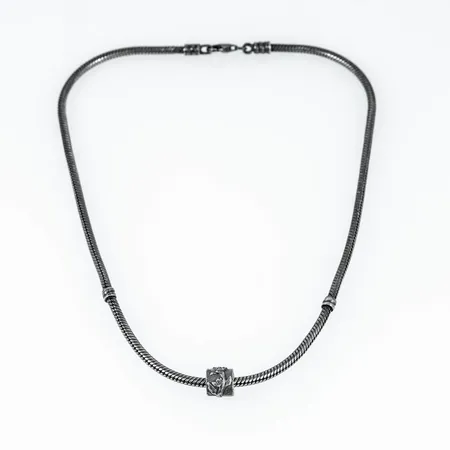 Pandora ormlänk i oxiderat silver med ett hänge. Den är 3 mm bred, hänget är 9,5 x 8 mm, och är 40 cm lång. Den väger 26,3g. Karbinhake.