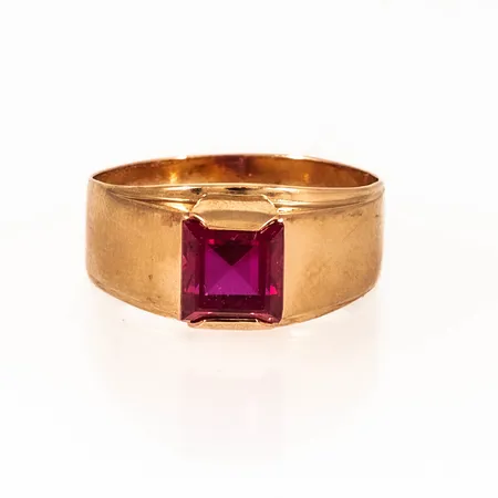 Ring i 18K guld med en knallröd, syntetisk spinell. Den är 3,8 - 8,3 mm bred, är i storlek 17¼ och väger 2,6g. Tillverkad 1976 av Ceson i Göteborg.