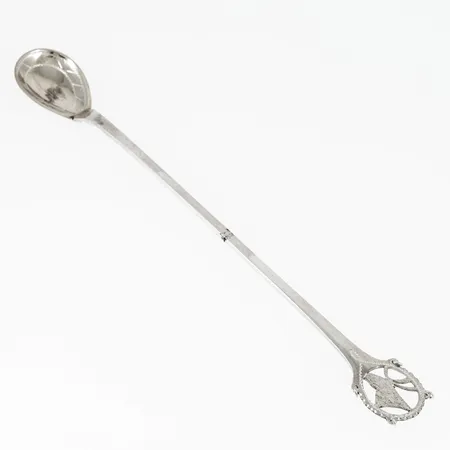 Sked med långt skaft i silver (830/1000) med samiskt mönster. Handsmide. Stämplad H9 (1958), LJG (Lindströms Juvel- och Guldsmedsaffär, Lycksele), S och kattfot. Vikt: 14,6g.