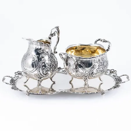 En gräddkanna höjd c:a 8 cm. En sockerskål höjd c:a 5,5 cm. Ett fat c:a 21 - 11,5 cm i silver. Total vikt: 430,3g. Stämplat N9 (1963) O9 (1964), GEWE (Gewe Silvervarufabriken AB, Malmö), S och kattfot.