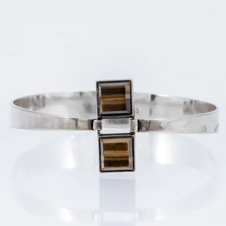 Armring i silver (813/1000) med två stenar (tigeröga). Innermått 18 cm, 60 x 52 mm. Den är 12 - 26 mm bred och väger 17,9g. Öppningsbar. Finska stämplar.