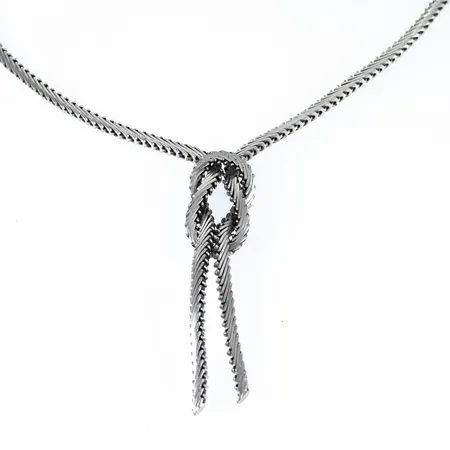 Colliér i silver (835/1000) med en knutdekor fram. Det är 45 cm långt, 3 mm brett och väger 20,0g. Längd på dekor 50 cm. Kistlås låses med säkerhetsåtta.